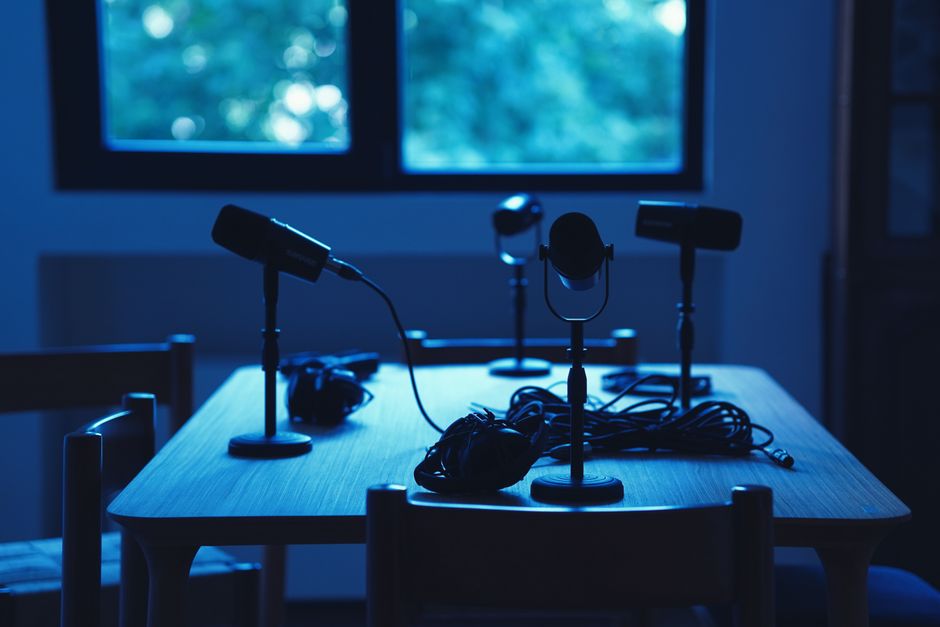 Dimly lit podcast studio with microphones and headphones on a table.