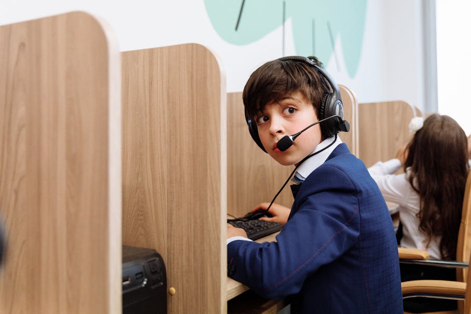 A boy in a blue suit wearing headphones focused in an educational setting with wooden cubicles.