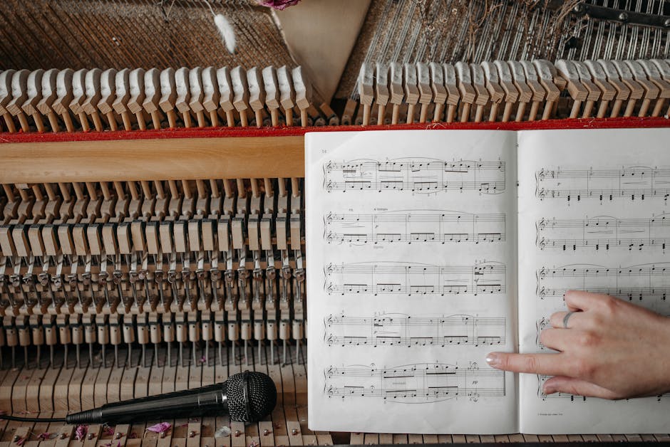 Closeup of piano interior and sheet music with hand pointing, microphone nearby.